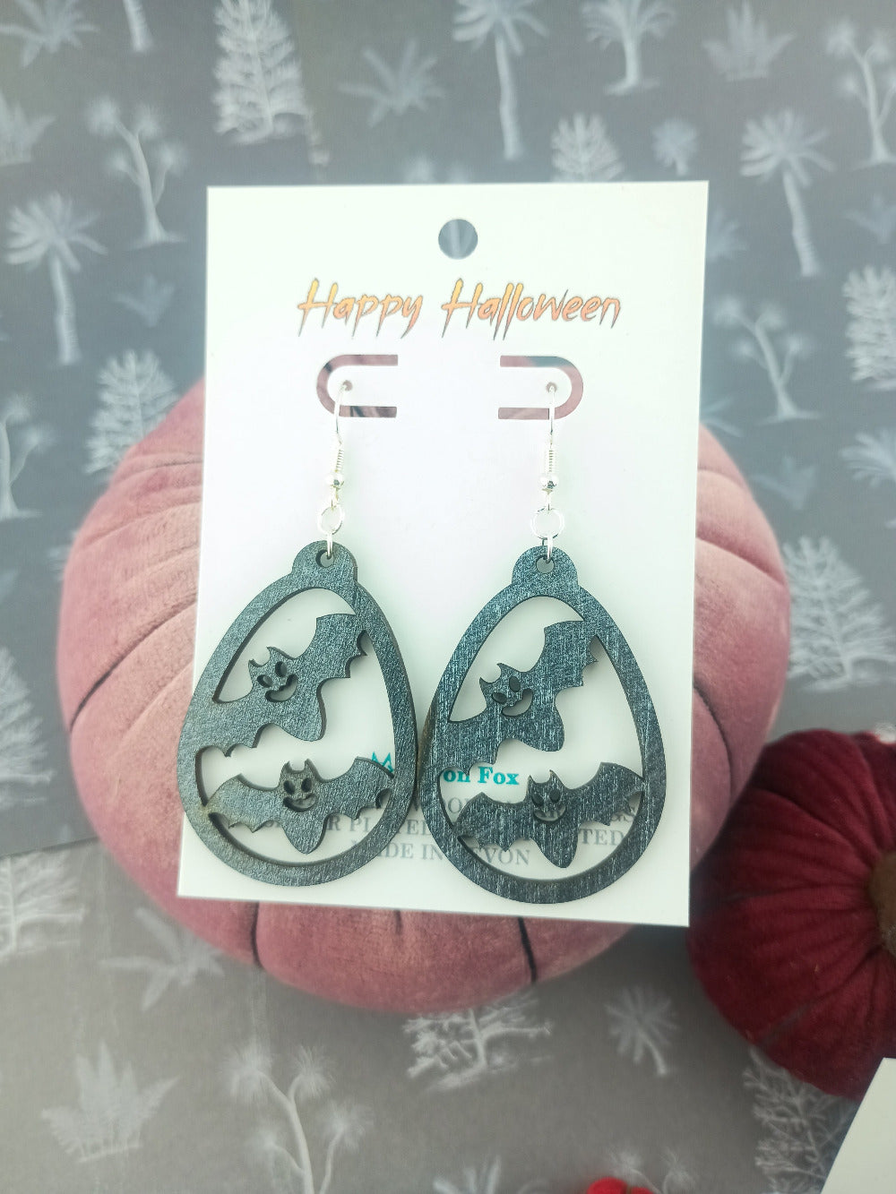 Bat-shaped earrings on a 'Happy Halloween' card