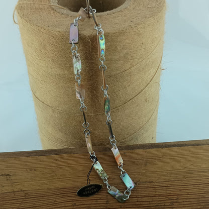 A handmade beaded necklace with silver-toned chain links and natural abalone shell beads in various colors, hanging from a spool of twine on a wooden surface.