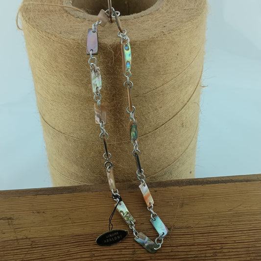 A handmade beaded necklace with silver-toned chain links and natural abalone shell beads in various colors, hanging from a spool of twine on a wooden surface.