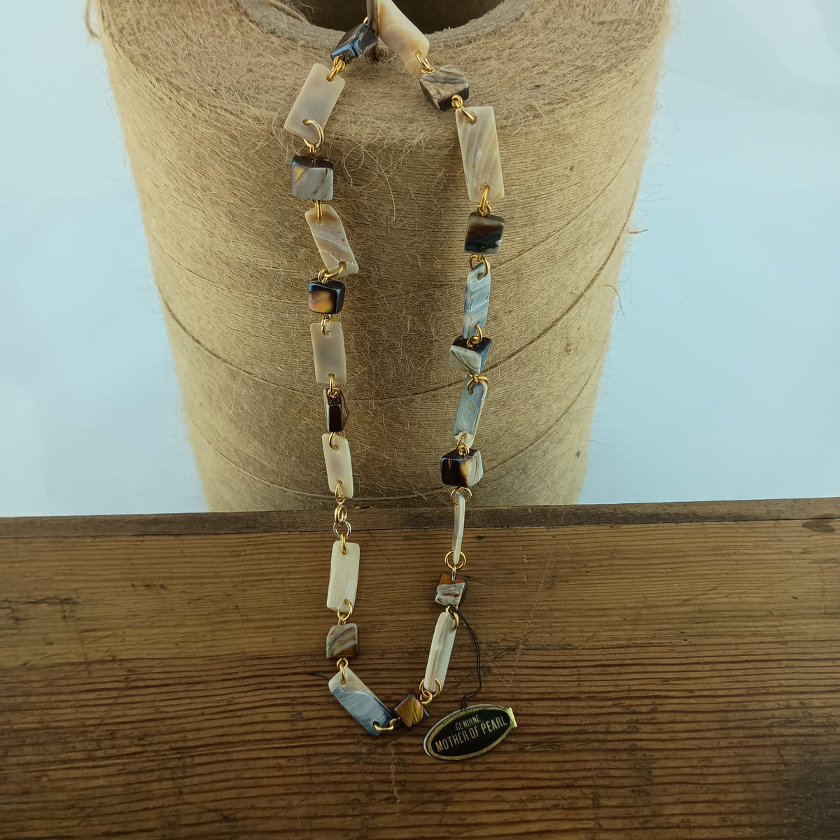 A beaded necklace with rectangular mother-of-pearl displayed on a spool of twine over a wooden surface.