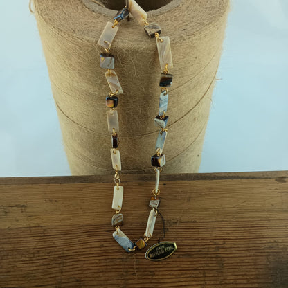 A beaded necklace with rectangular mother-of-pearl displayed on a spool of twine over a wooden surface.