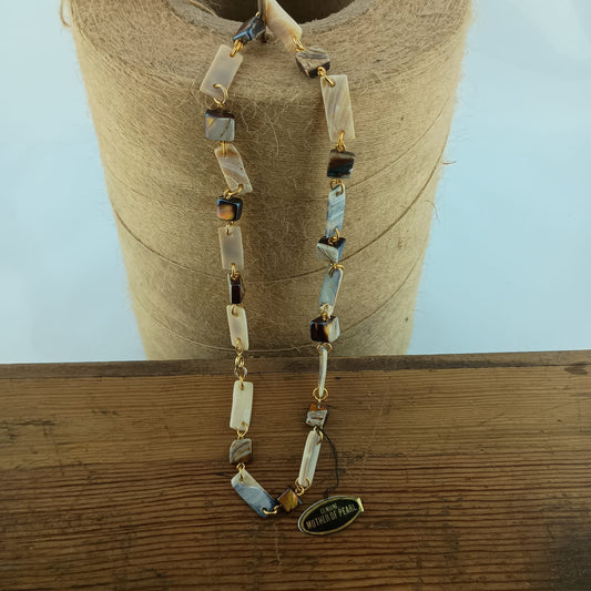 A beaded necklace with rectangular mother-of-pearl displayed on a spool of twine over a wooden surface.