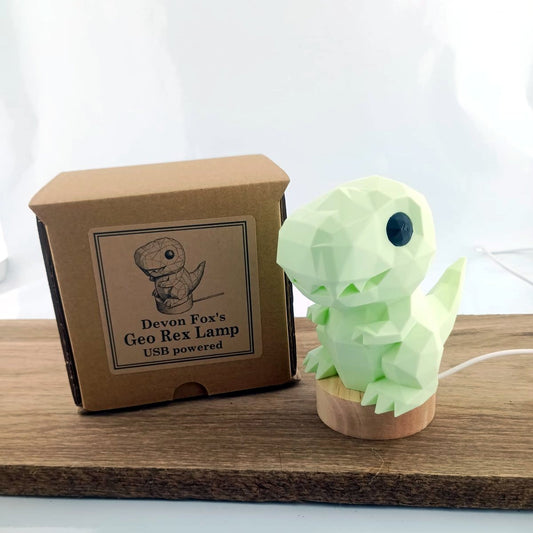Green dinosaur-shaped lamp next to its packaging box on a wooden surface.