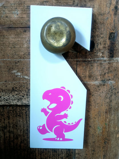 White door hanger with pink dinosaur design and gold knob on wooden surface